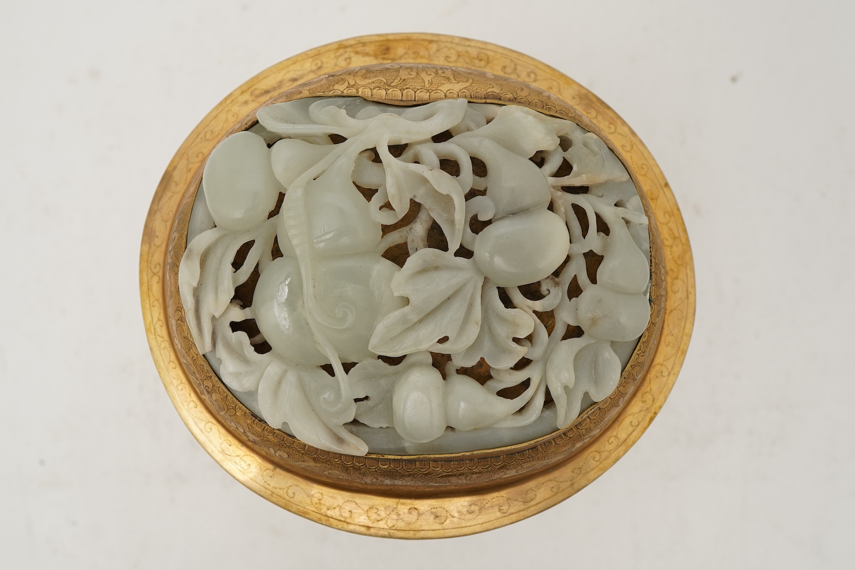 A Chinese pale celadon jade oval plaque, 17th/18th century, mounted on a late Qing gilt copper jar